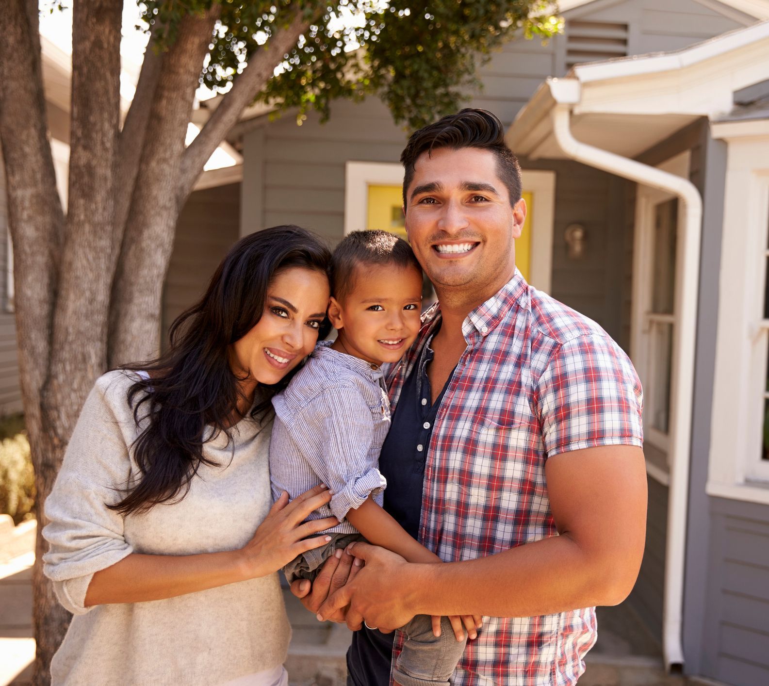 A smiling couple with their child standing in front of their home, representing the advantages of equity lines of credit.